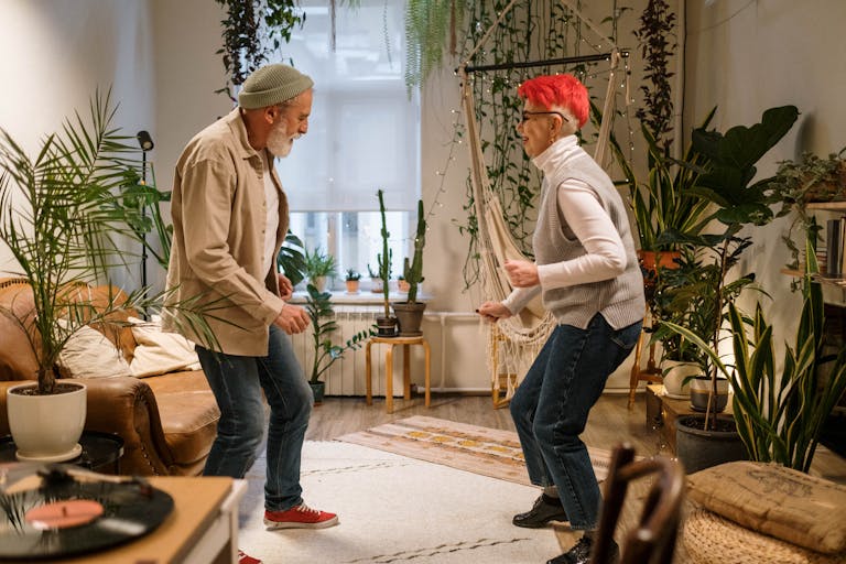 Energetic senior couple dancing together at home surrounded by indoor plants.